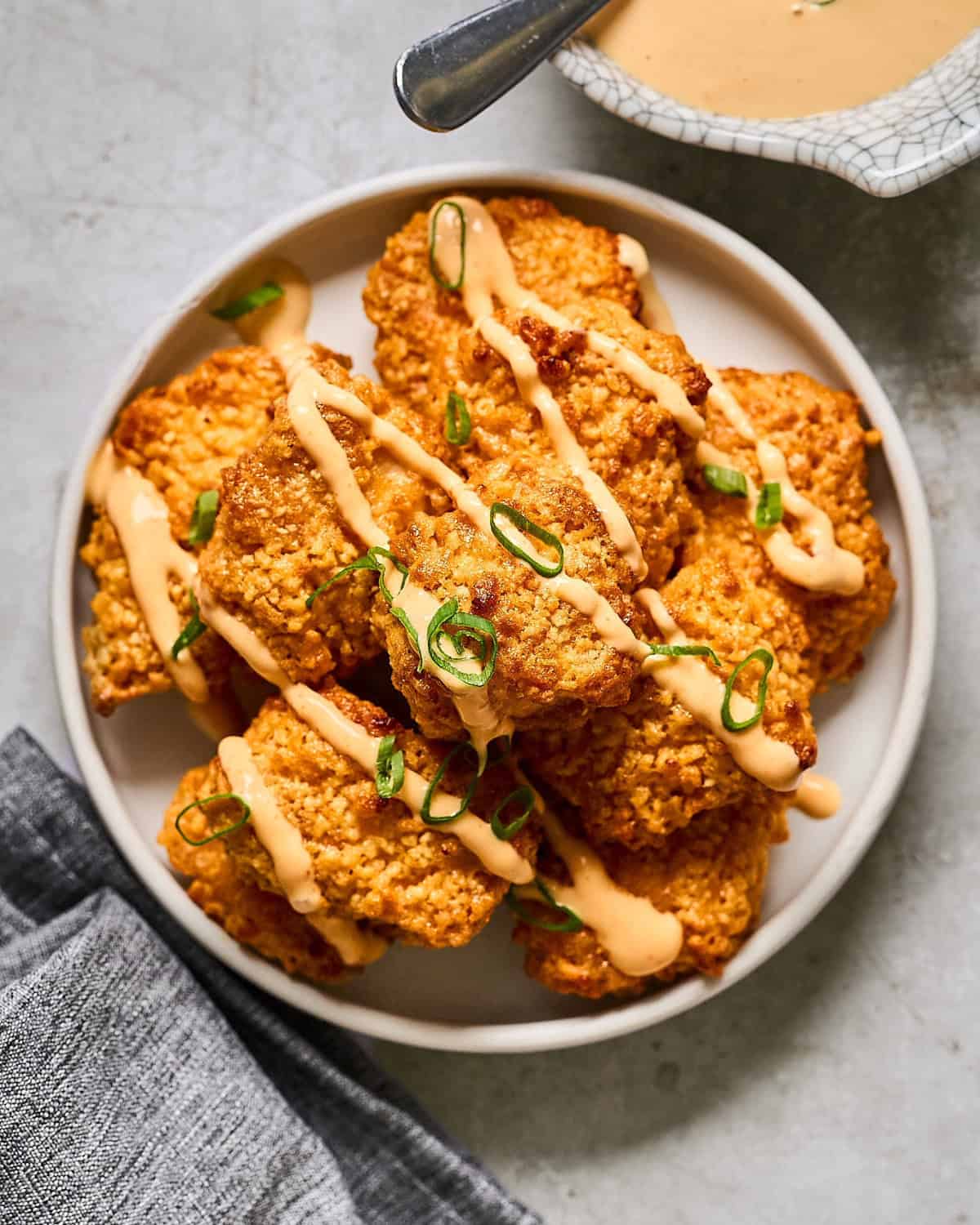 oven baked bang bang chicken pieces on a white plate drizzled with bang bang sauce and green onions.