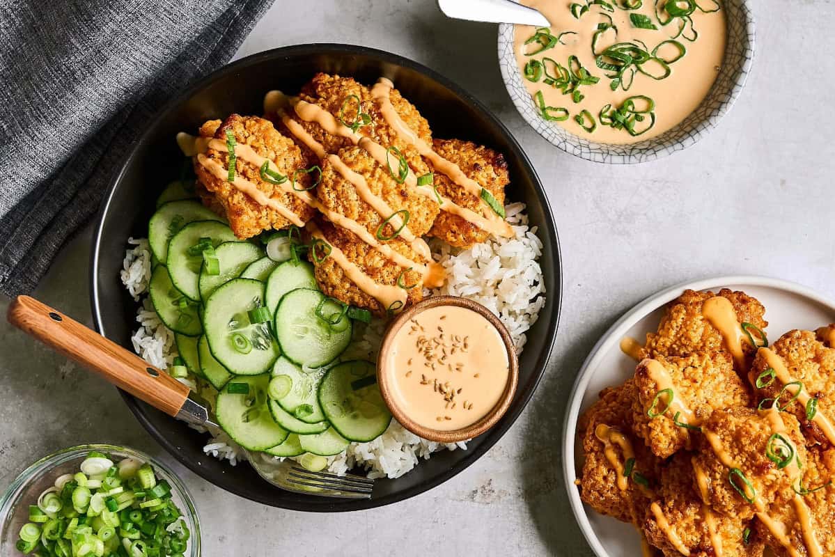 Bang bang chicken served in a bowl of rice with cucumbers and bang bang sauce.