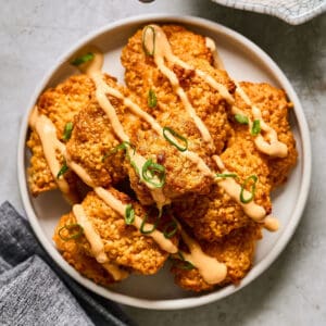 oven baked bang bang chicken pieces on a white plate drizzled with bang bang sauce and green onions.