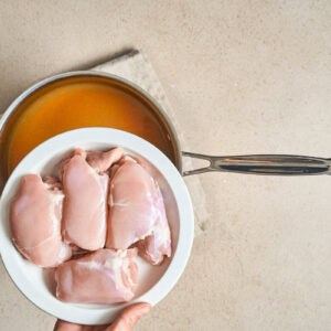 raw chicken thighs on a plate over a pot.