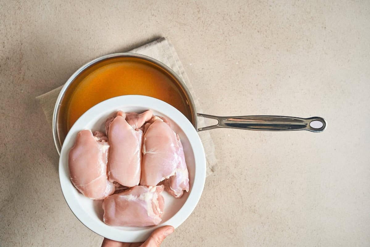 raw chicken thighs on a plate over a pot.