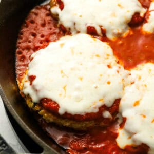 Breaded chicken burger patties, coated in marinara sauce and cheese, in a cast iron skillet.