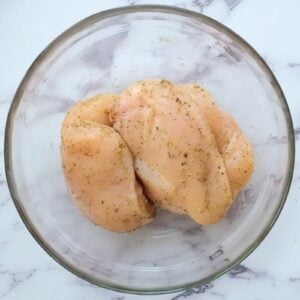 Seasoned chicken breasts in a glass bowl.
