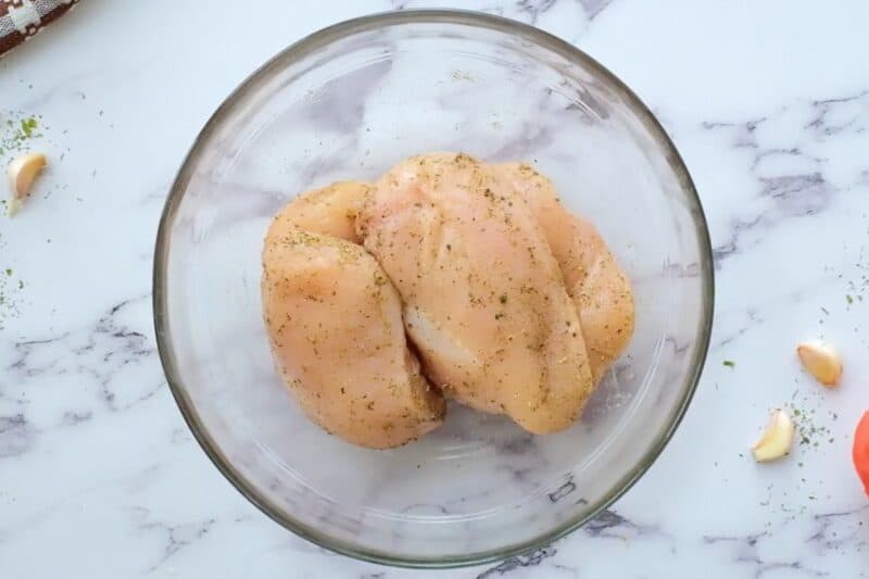 Seasoned chicken breasts in a glass bowl.