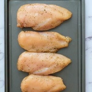 Seasoned chicken breasts lined up on a sheet pan.