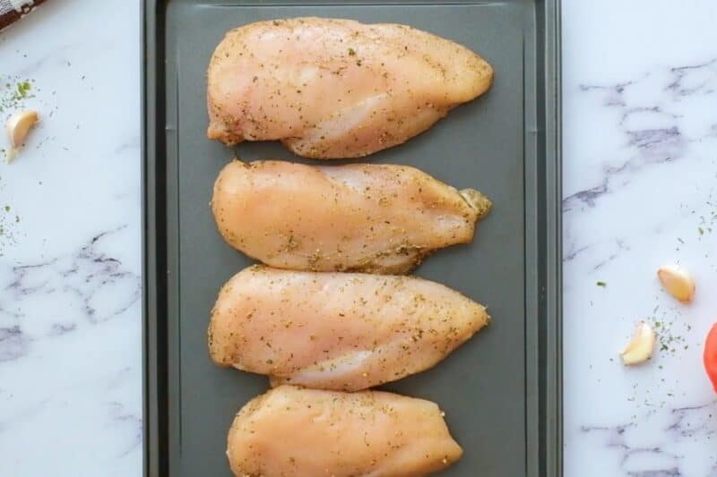 Seasoned chicken breasts lined up on a sheet pan.