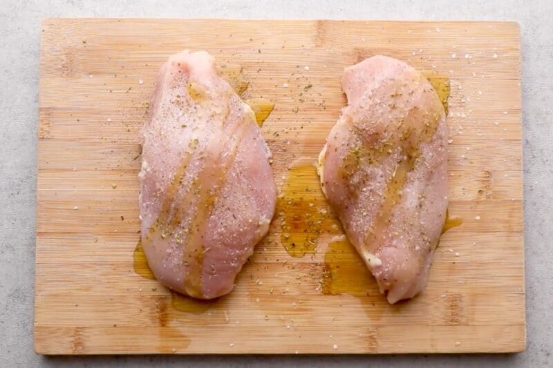 Raw chicken breasts on a cutting board, coated with olive oil and Italian seasoning.