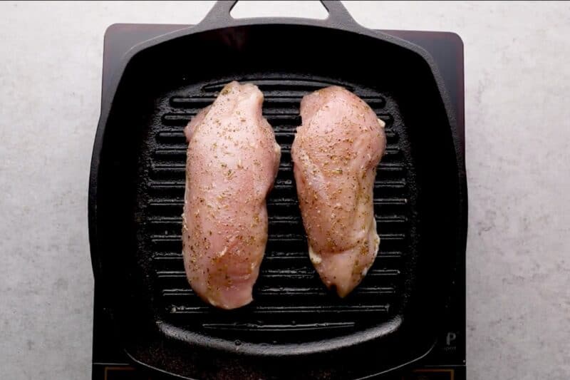 Seasoned chicken breasts cooking on a grill pan.