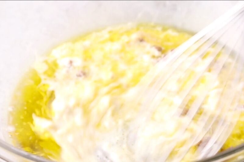 Whisking caesar salad dressing ingredients together in a bowl.