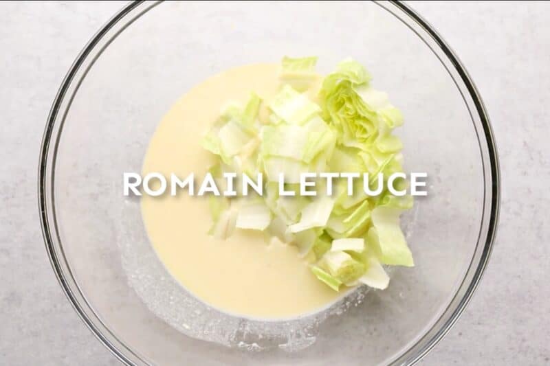 Chopped romaine lettuce added to a bowl of caesar dressing.
