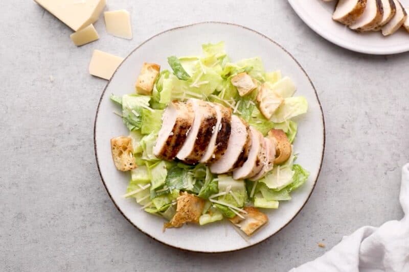 A plated Caesar salad topped with sliced grilled chicken breast and baked croutons.