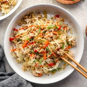 Chicken egg roll in a bowl garnished with green onion, sriracha and sesame seeds.