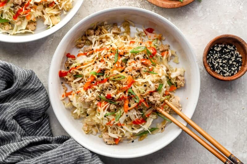 Chicken egg roll in a bowl garnished with green onion, sriracha and sesame seeds.