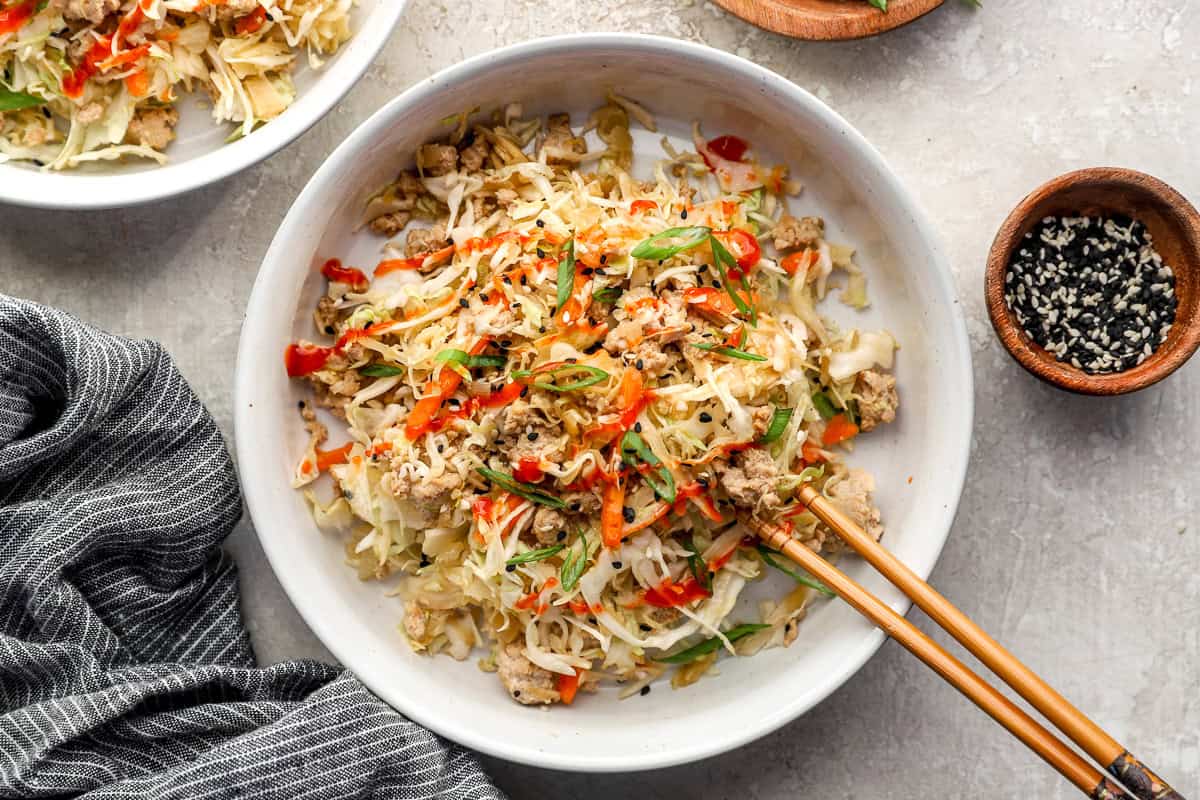 Chicken egg roll in a bowl garnished with green onion, sriracha and sesame seeds.