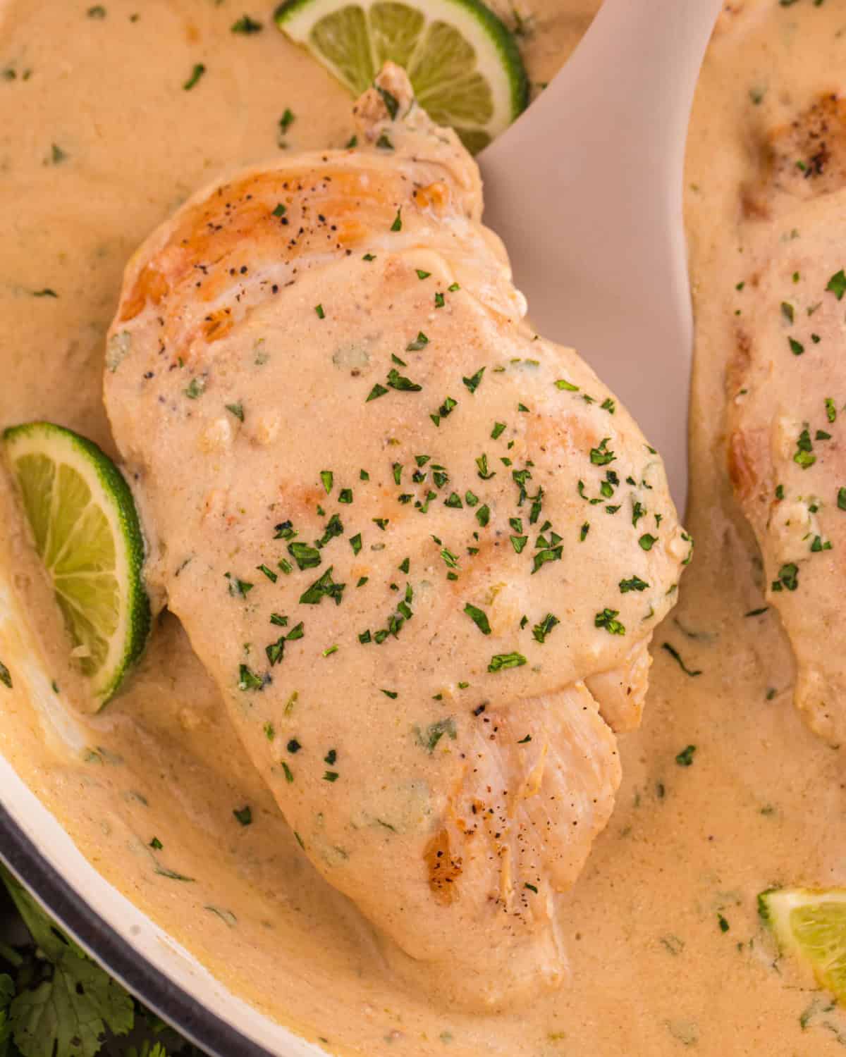 Spatula lifting up a chicken breast coated in a creamy coconut lime sauce.