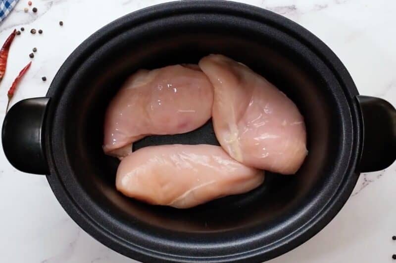 Raw chicken breasts in a slow cooker.