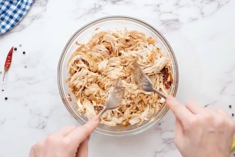 Shredding chicken in a bowl, using two forks.