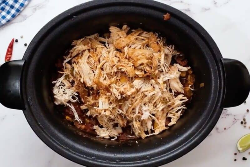 Shredded chicken added to a slow cooker filled with salsa, black beans, and corn.