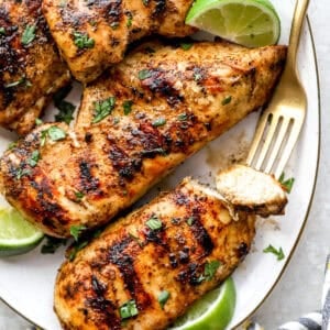 A plate of grilled chicken breast, with a fork holding a piece of chicken.