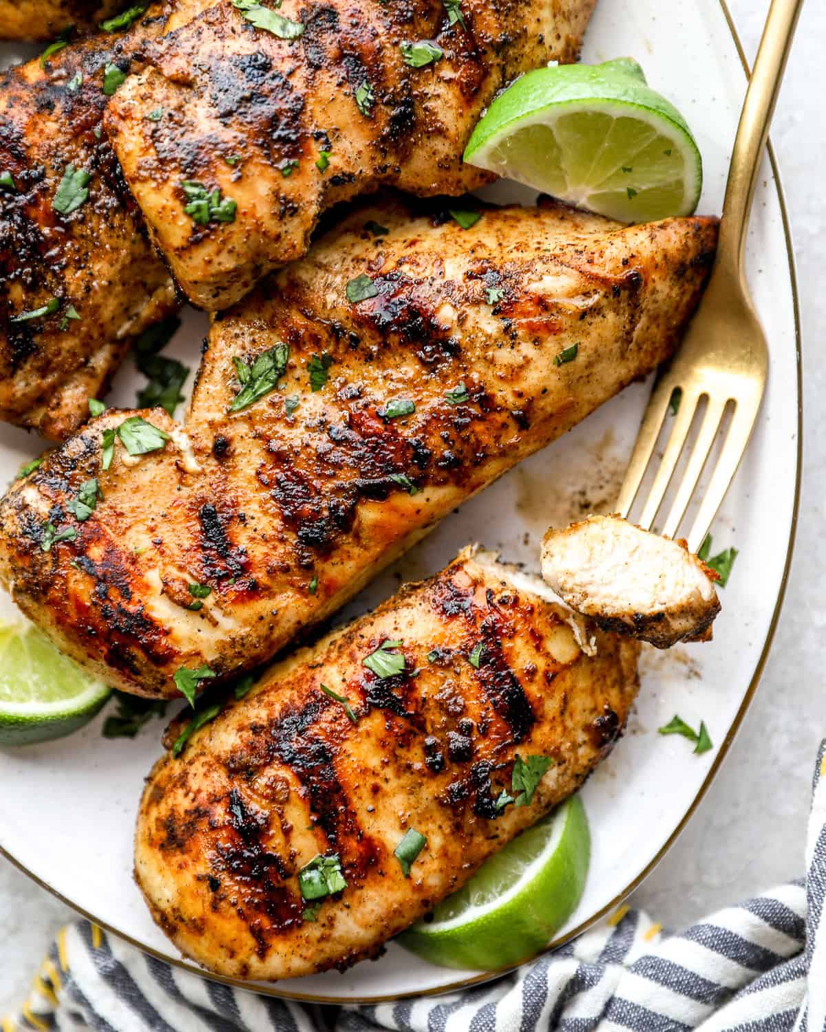 A plate of grilled chicken breast, with a fork holding a piece of chicken.