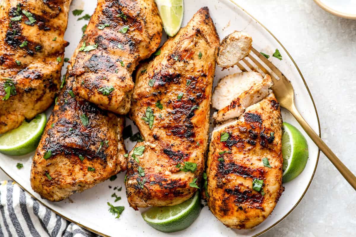 A plate of grilled chicken breasts, one partially cut into pieces.