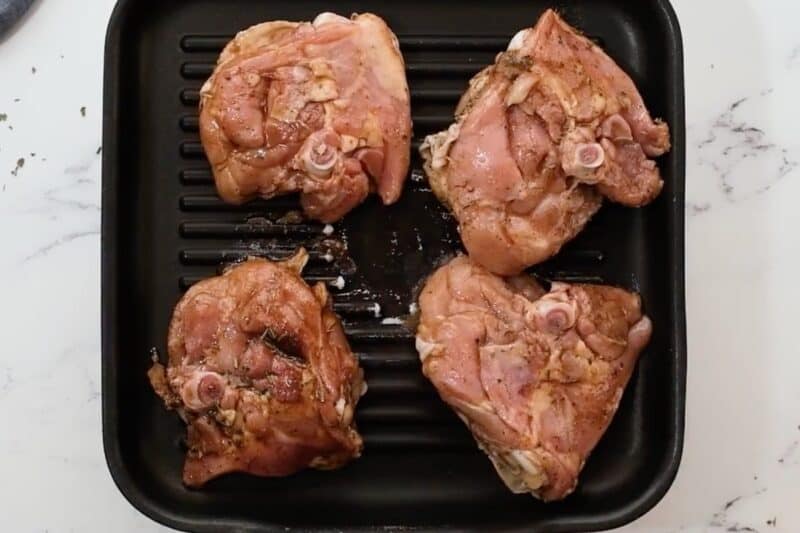Marinated chicken thighs on a grill.