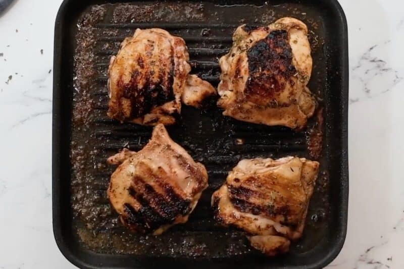 Marinated chicken thighs cooking on a grill.