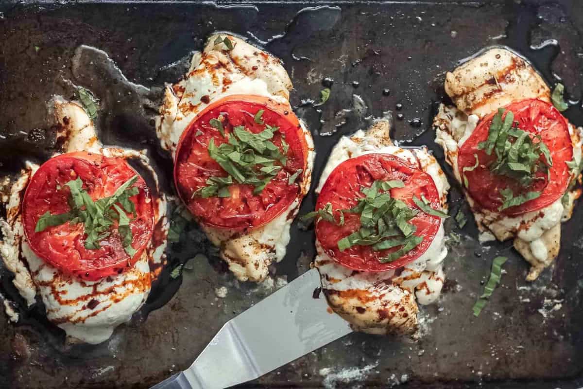 Caprese chicken on a sheet pan, garnished with basil and balsamic.