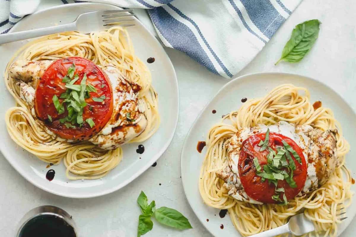 Caprese chicken served on plates of spaghetti.