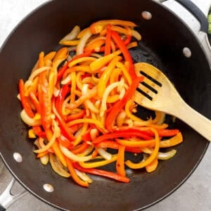 Onions and bell peppers being cooked in a skillet.