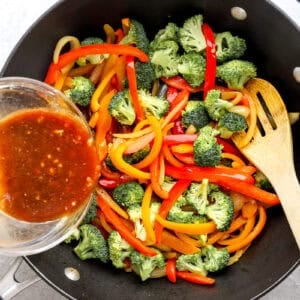 Stir fry sauce being poured over vegetables in a skillet.