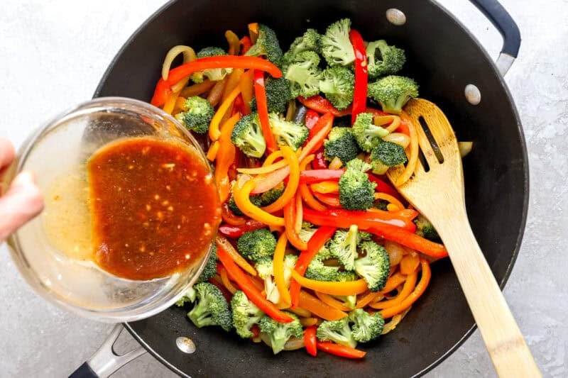 Stir fry sauce being poured over vegetables in a skillet.