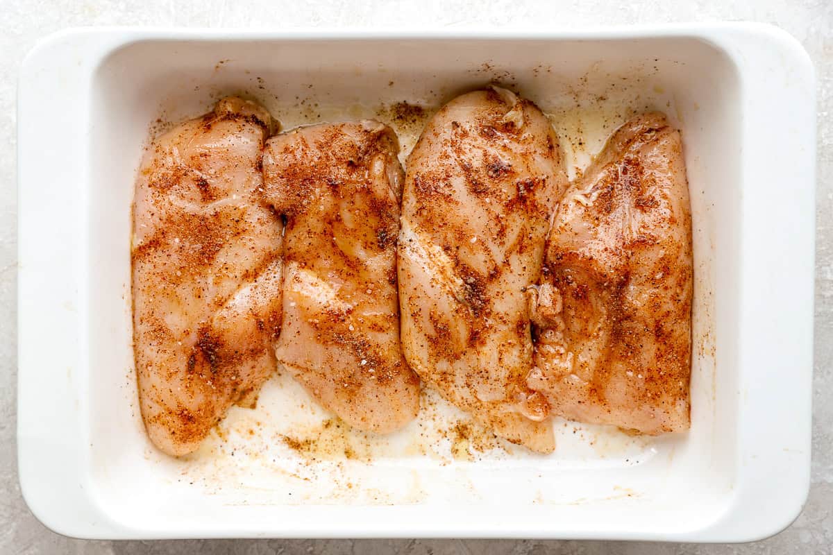 Raw chicken breasts coated in seasoning blend, marinating in a dish.