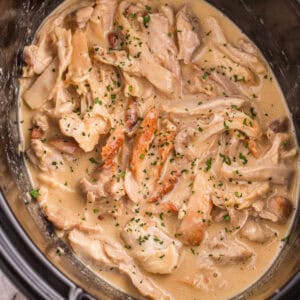 Cooked chicken thighs in a sauce in a slow cooker garnished with fresh herbs.