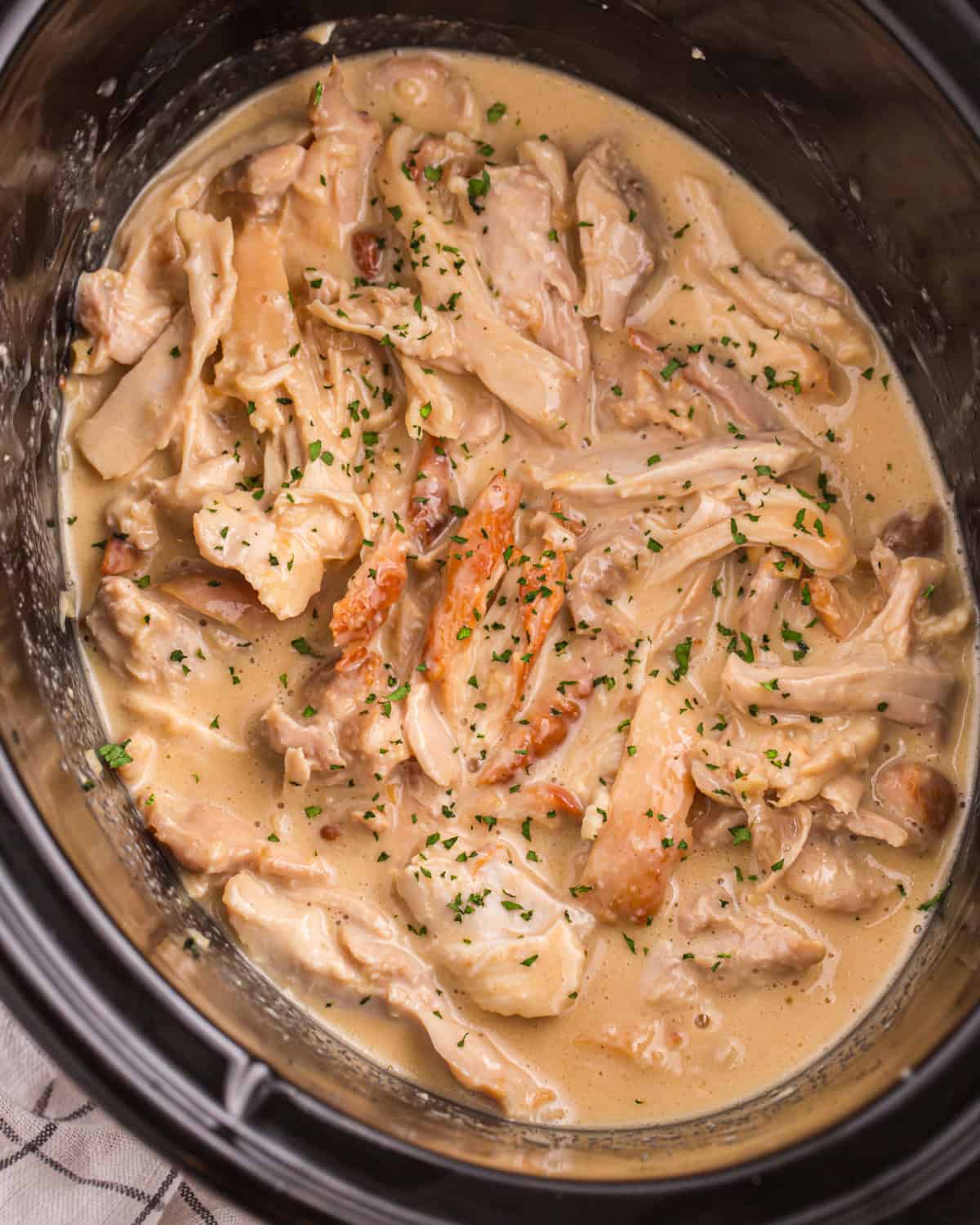 Shredded honey mustard chicken thighs in a slow cooker, garnished with fresh herbs.