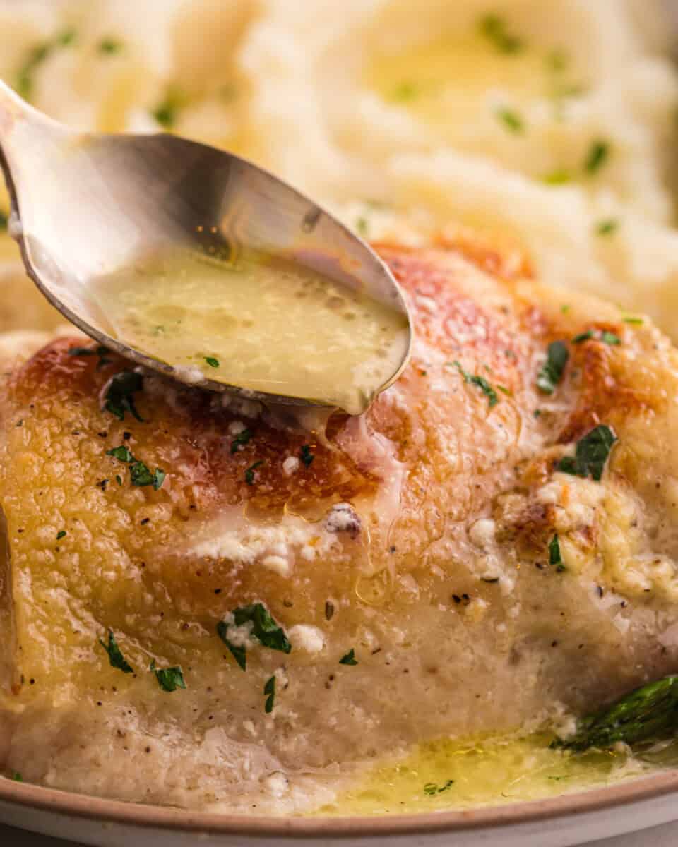 Spooning buttery sauce over baked chicken thighs.