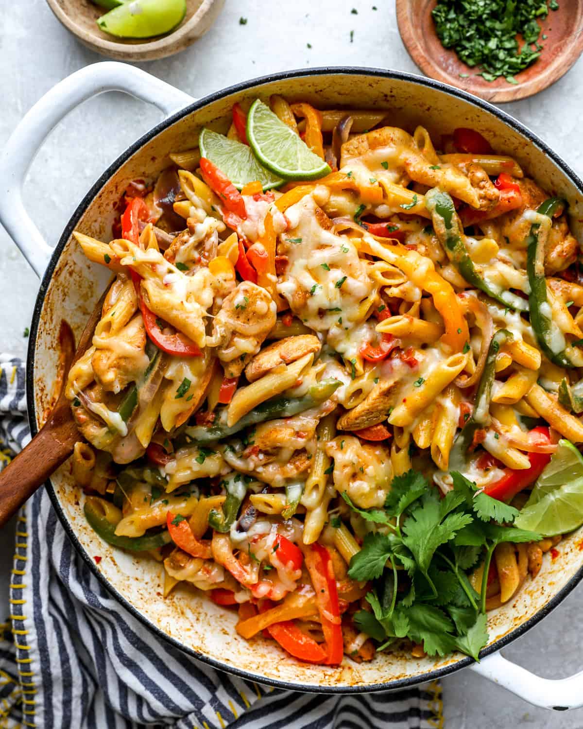 Creamy chicken fajita pasta in a skillet garnished with cilantro and lime wedges.
