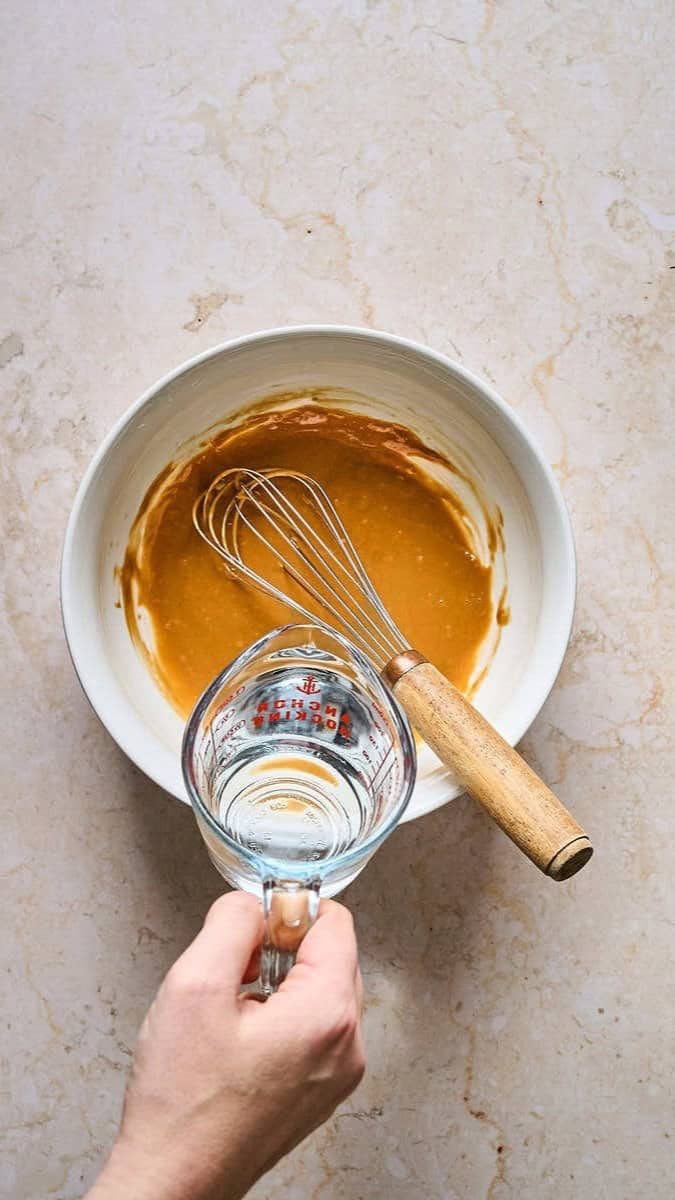 Pouring water into tahini dressing to get the right consistency.