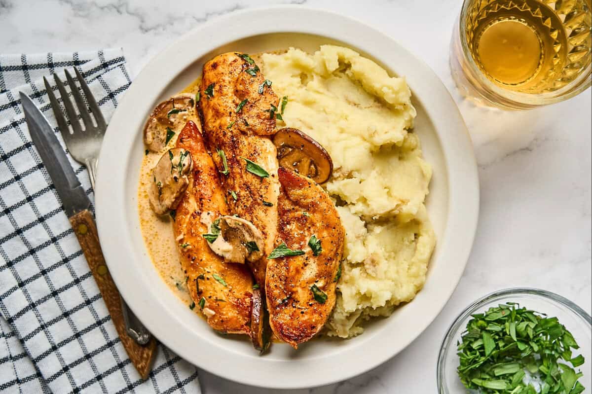 A serving of tarragon chicken with cream sauce, mushrooms, and mashed potatoes.
