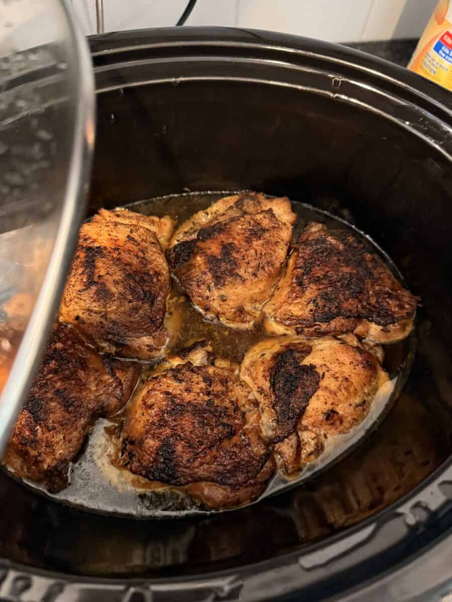 Lifting lid to show chicken thighs cooking in Crock Pot.