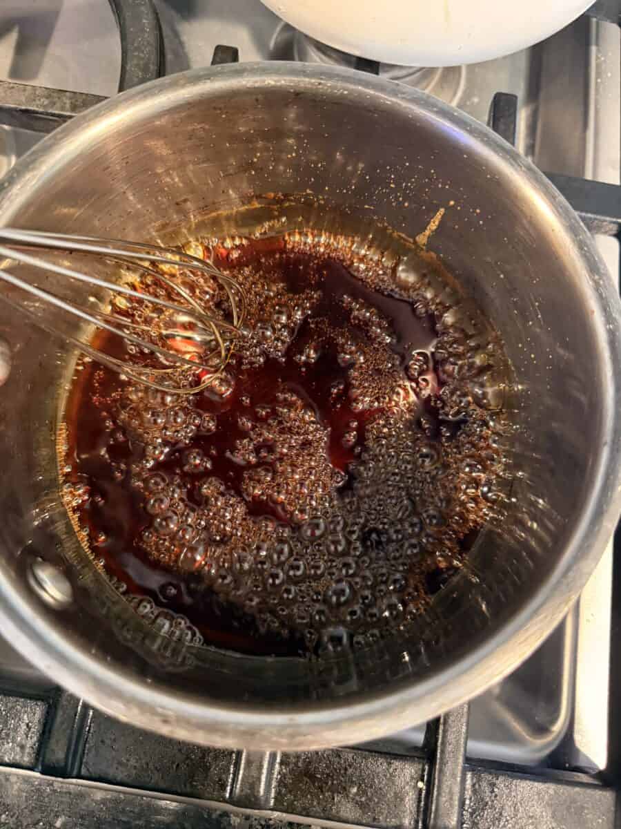 Whisking sauce as it boils in a saucepan on the stovetop.