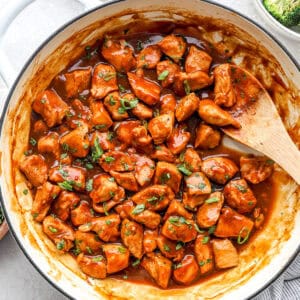 Chicken pieces in a thick diet coke sauce in a skillet garnished with fresh herbs.