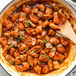 Chicken pieces in a diet coke sauce being stirred in a skillet.