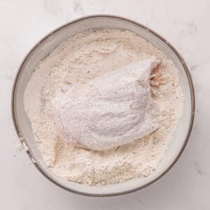 Chicken being coated in the flour mixture.