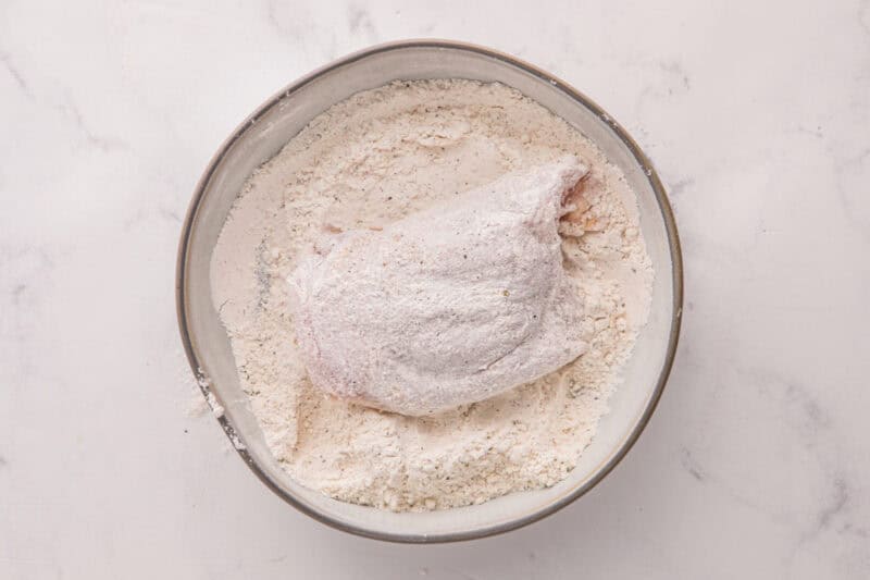 Chicken being coated in the flour mixture.