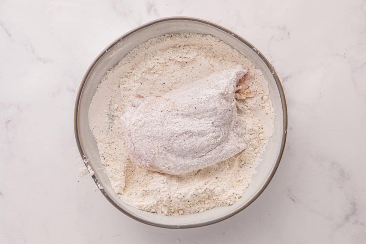 Dredging chicken thigh in flour.