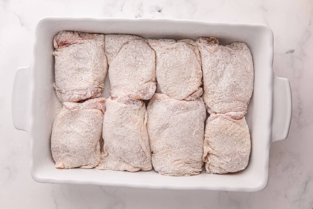 Dredged bone-in chicken thighs lined up in a baking pan.