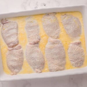 Chicken thighs and broth in a baking dish.