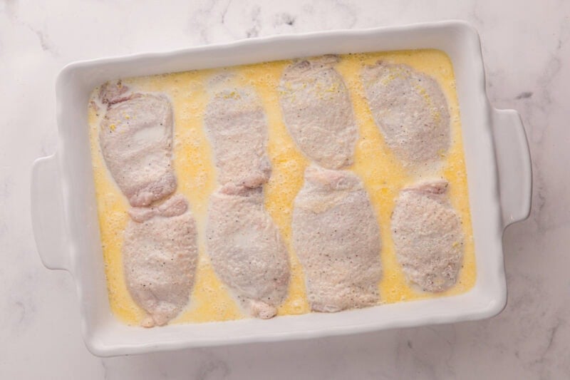 Chicken thighs and broth in a baking dish.
