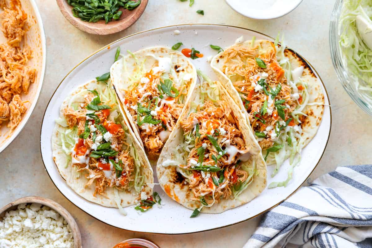 Four buffalo chicken tacos on a white serving plate.